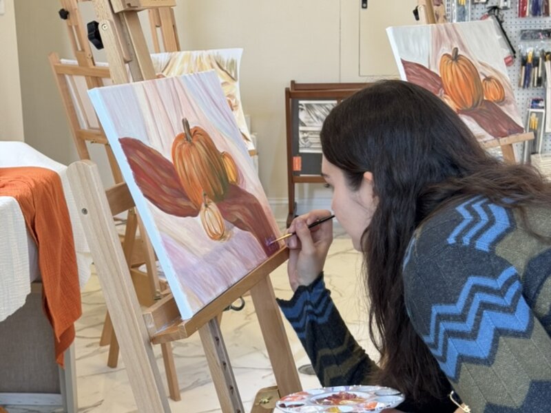 Guest painting pumpkins on canvas at an easel