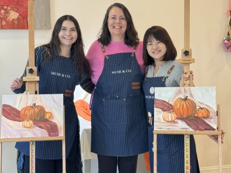 Three artists holding pumpkin paintings inside Muse & Co
