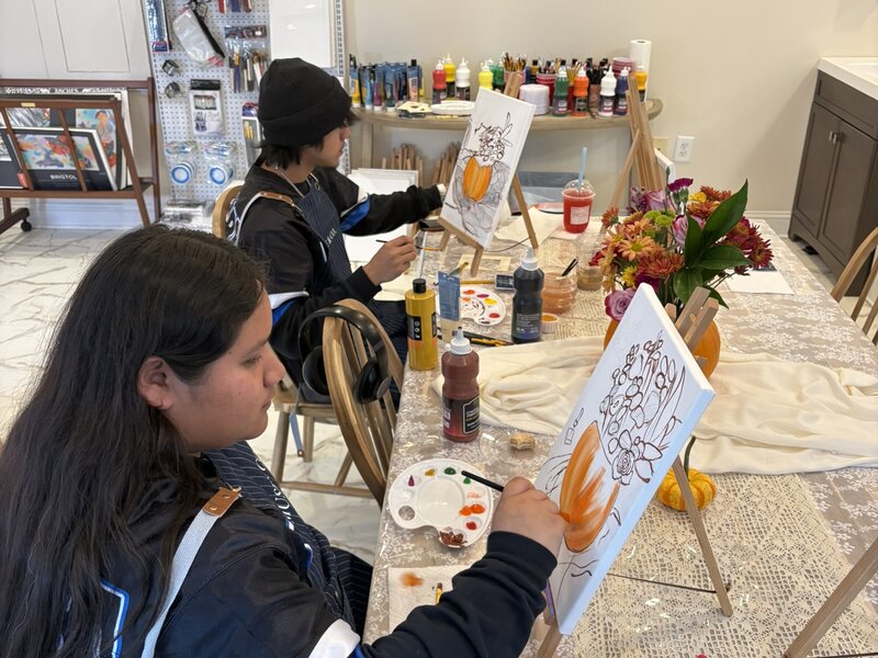 Two guests painting pumpkin canvases at a shared table